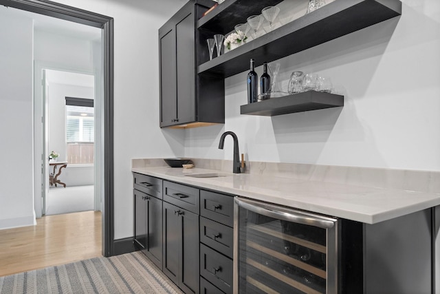 bar featuring wine cooler, baseboards, a sink, indoor wet bar, and light wood-type flooring