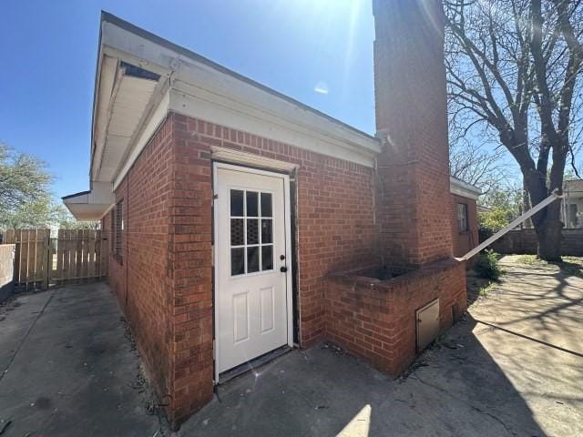 exterior space with brick siding, a chimney, fence, and a patio area