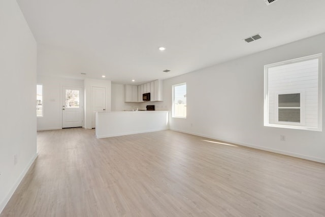 unfurnished living room featuring light wood-type flooring, a wealth of natural light, baseboards, and visible vents