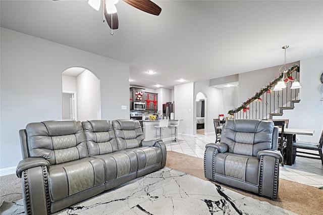 living room featuring ceiling fan, light tile patterned floors, stairway, and arched walkways