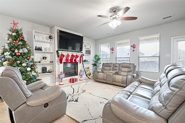 living room featuring a wealth of natural light, visible vents, a ceiling fan, and a glass covered fireplace