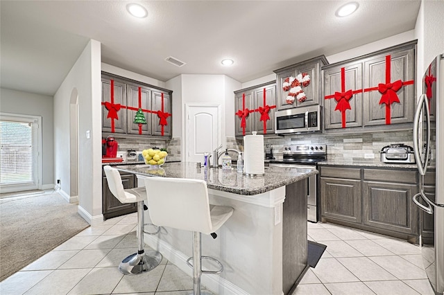 kitchen with tasteful backsplash, light stone counters, a kitchen island with sink, light tile patterned floors, and appliances with stainless steel finishes