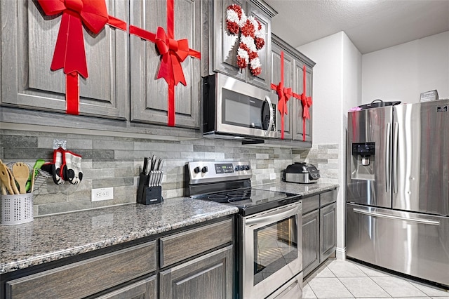 kitchen with stainless steel appliances, backsplash, light tile patterned flooring, and dark stone countertops