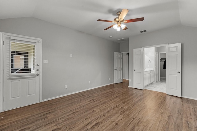 unfurnished bedroom featuring ensuite bath, vaulted ceiling, wood finished floors, and baseboards