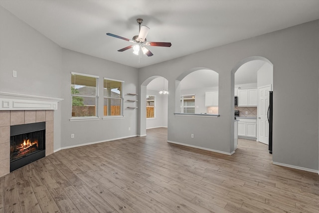 unfurnished living room with a ceiling fan, light wood-style floors, a tile fireplace, and baseboards
