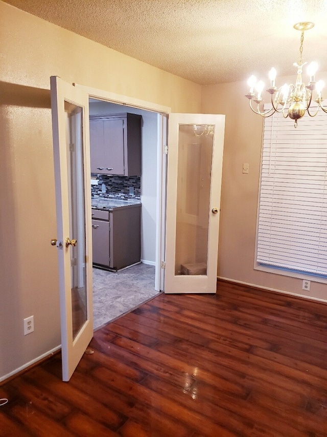 empty room featuring french doors, wood finished floors, a chandelier, a textured ceiling, and baseboards