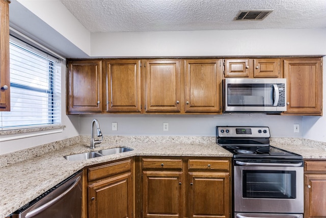 1200 Harwell Dr Unit 1924, Arlington, TX 76011 - kitchen featuring appliances with stainless steel finishes, a sink, a textured ceiling, light stone counters, and brown cabinets