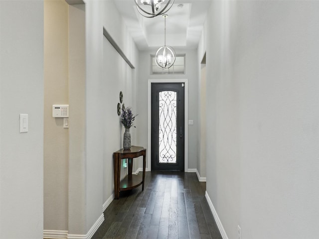 foyer entrance featuring a raised ceiling, a notable chandelier, baseboards, and dark wood finished floors