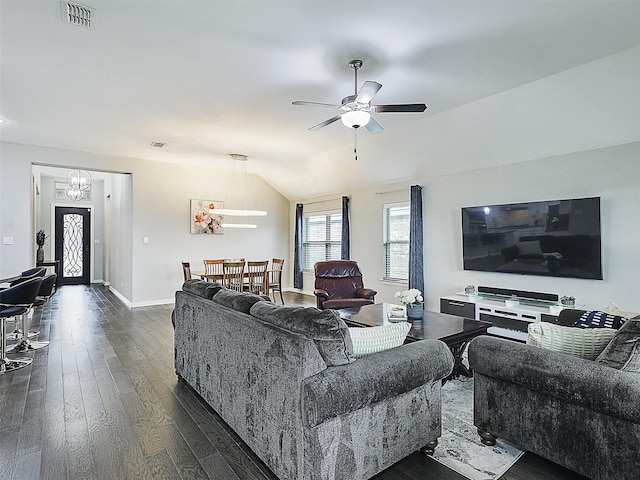 living area with ceiling fan with notable chandelier, visible vents, baseboards, dark wood-type flooring, and vaulted ceiling