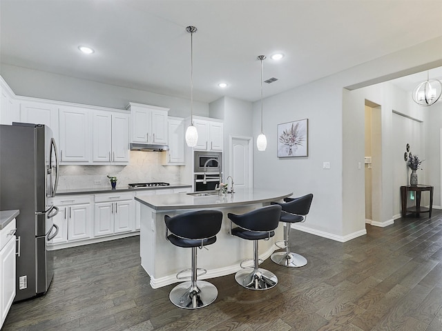 kitchen with under cabinet range hood, a breakfast bar, dark wood-type flooring, stainless steel appliances, and tasteful backsplash