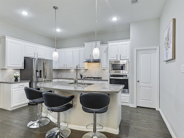 kitchen with a kitchen bar, a sink, stainless steel appliances, white cabinets, and tasteful backsplash