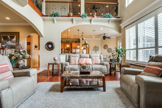 living area with ceiling fan, a towering ceiling, and ornamental molding