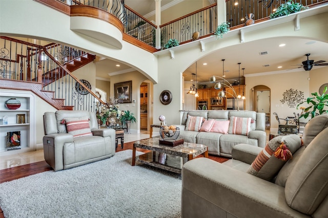 living area featuring ornamental molding, a towering ceiling, ceiling fan with notable chandelier, and arched walkways