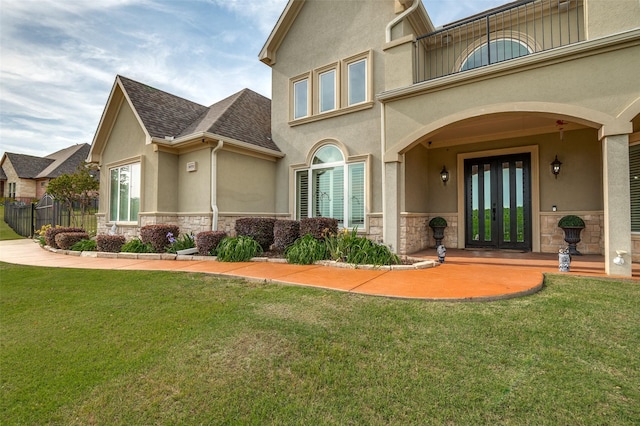 property entrance with a yard, stone siding, stucco siding, and french doors