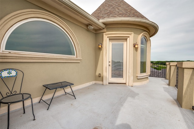 entrance to property featuring stucco siding, roof with shingles, and a patio