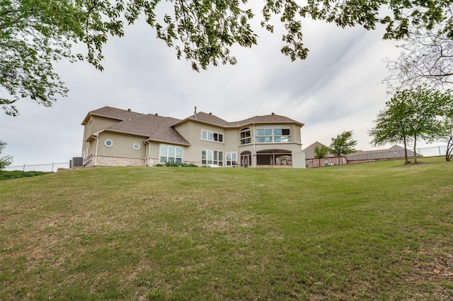 back of house with central air condition unit, fence, stucco siding, and a yard