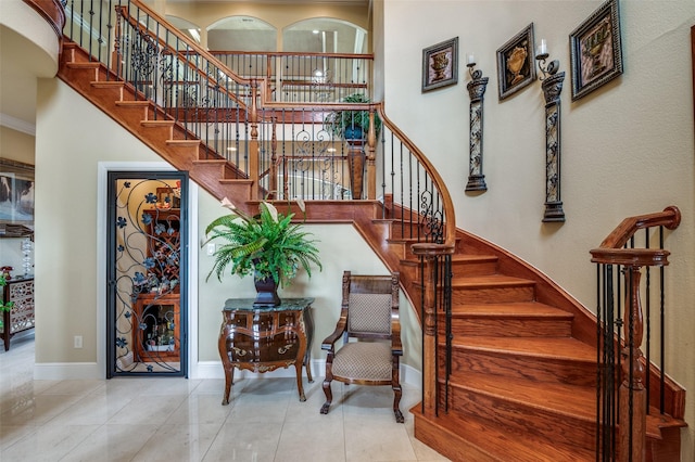 stairway with baseboards, tile patterned flooring, a towering ceiling, and ornamental molding