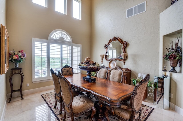 dining area featuring light tile patterned floors, visible vents, baseboards, and a towering ceiling