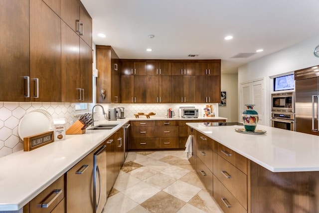 kitchen with a center island, a sink, built in appliances, light countertops, and tasteful backsplash
