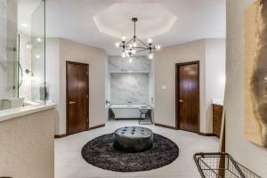 full bathroom featuring a raised ceiling, walk in shower, a soaking tub, and a chandelier