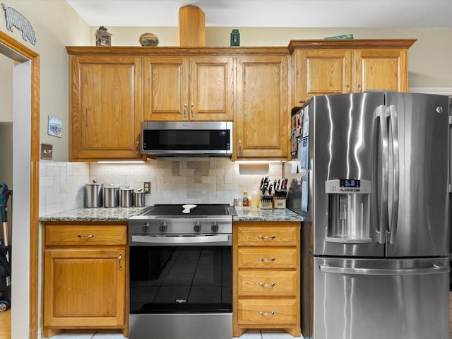 kitchen featuring brown cabinets, light stone countertops, tasteful backsplash, and appliances with stainless steel finishes