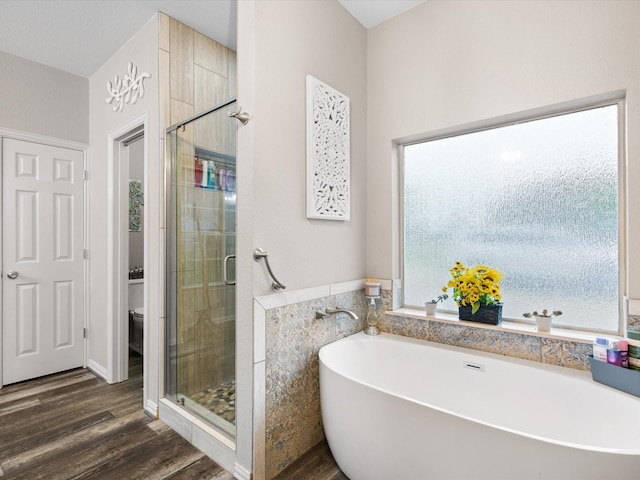 bathroom with a freestanding bath, toilet, a shower stall, and wood finished floors