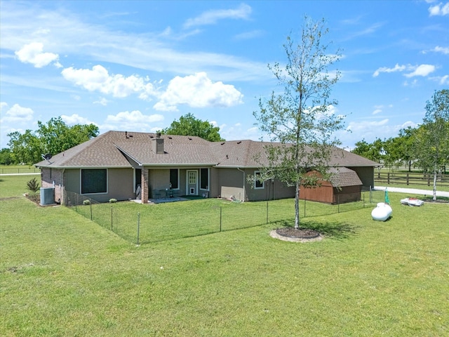 back of property featuring a yard, an outbuilding, a shingled roof, and fence