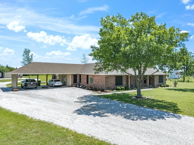 ranch-style home featuring a carport, a front yard, brick siding, roof with shingles, and gravel driveway