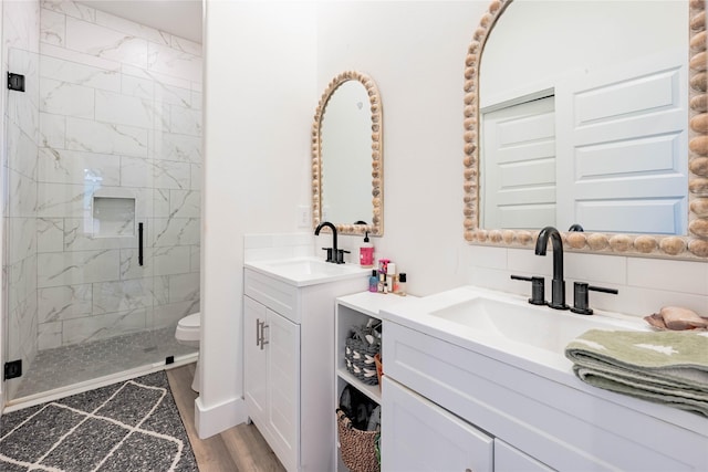 full bathroom featuring toilet, a stall shower, two vanities, and a sink