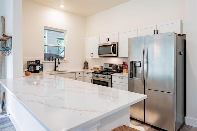 kitchen with light stone countertops, a sink, a peninsula, stainless steel appliances, and white cabinets