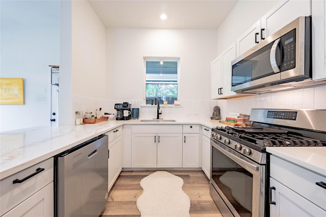 kitchen featuring light stone countertops, a sink, light wood-style floors, stainless steel appliances, and tasteful backsplash