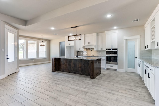 kitchen featuring double oven, tasteful backsplash, visible vents, and under cabinet range hood