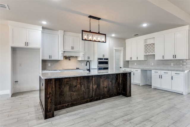kitchen featuring backsplash, double oven, white cabinets, and light wood-type flooring