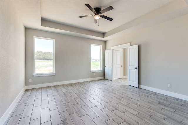 empty room featuring baseboards, wood finished floors, a raised ceiling, and ceiling fan