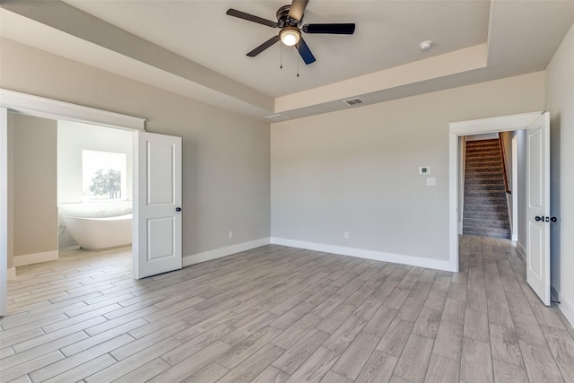 unfurnished room featuring a ceiling fan, light wood-style floors, a tray ceiling, and baseboards
