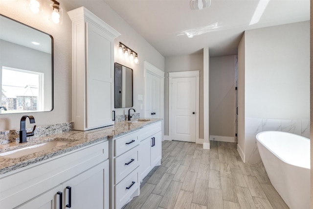 full bathroom featuring double vanity, wood finished floors, a freestanding bath, and a sink