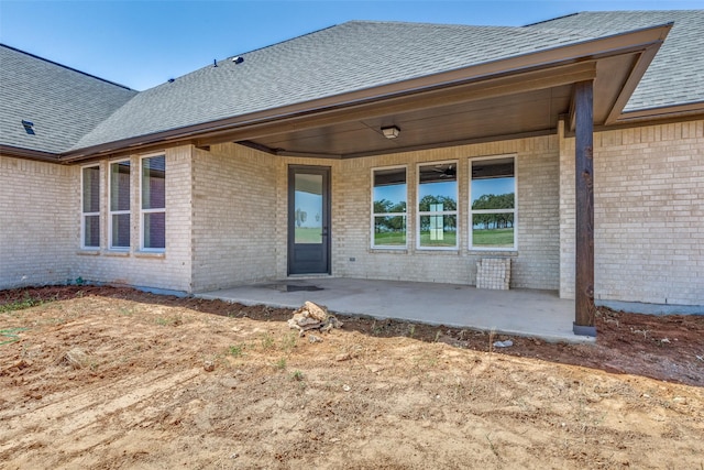 back of property with brick siding, roof with shingles, and a patio area