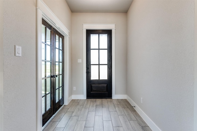 doorway to outside with light wood-type flooring, a textured wall, baseboards, and french doors