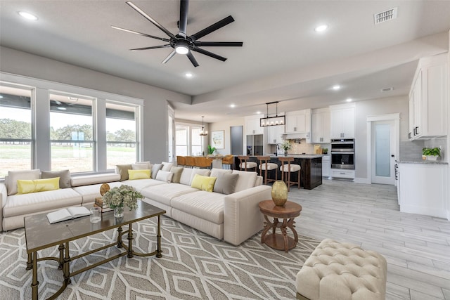 living room with light wood-style floors, ceiling fan with notable chandelier, visible vents, and recessed lighting