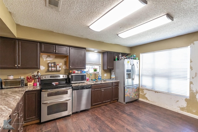 kitchen with stainless steel appliances, dark wood-style flooring, a textured ceiling, baseboards, and dark brown cabinetry