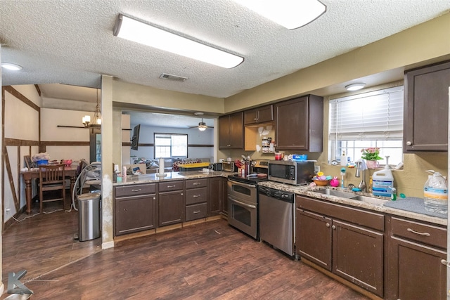 kitchen with appliances with stainless steel finishes, a sink, a textured ceiling, dark brown cabinets, and dark wood finished floors