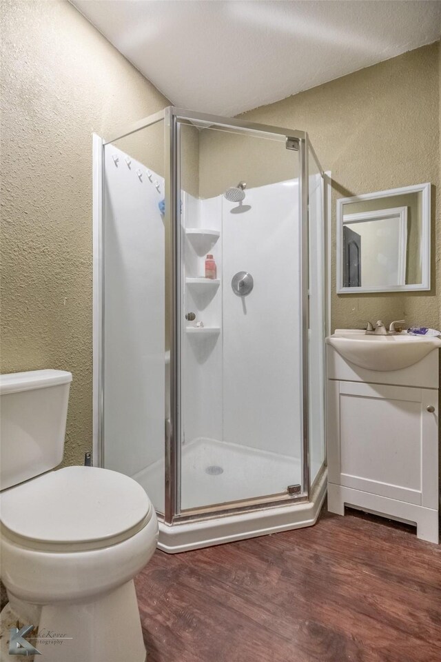 bathroom featuring a textured wall, wood finished floors, vanity, toilet, and a stall shower