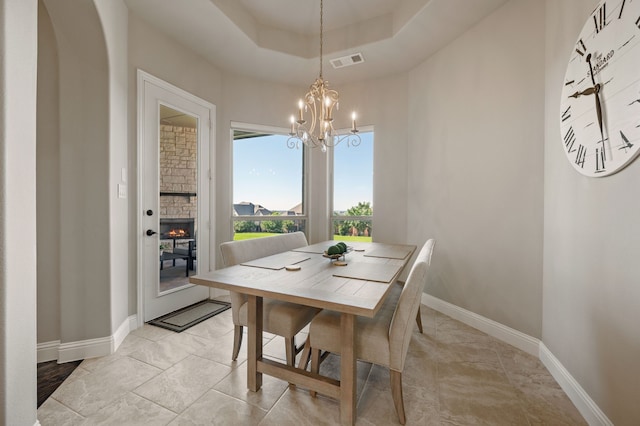 dining room featuring a chandelier, a fireplace, baseboards, and a tray ceiling