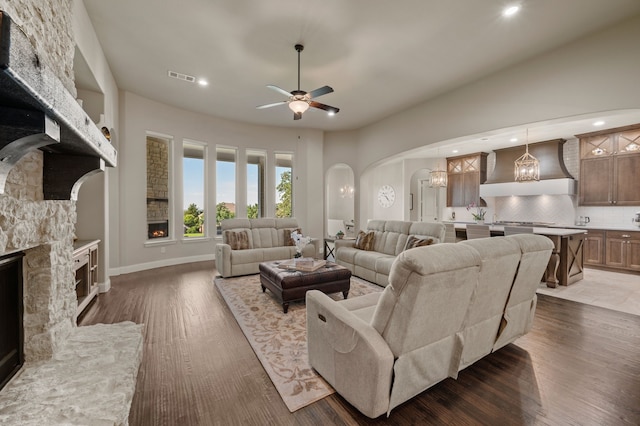 living area with arched walkways, a fireplace, ceiling fan, dark wood-type flooring, and recessed lighting