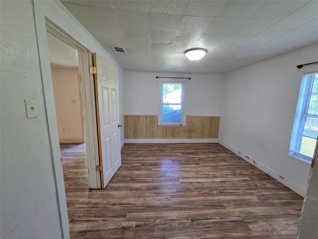 unfurnished room with dark wood-style flooring, wooden walls, visible vents, and a wainscoted wall