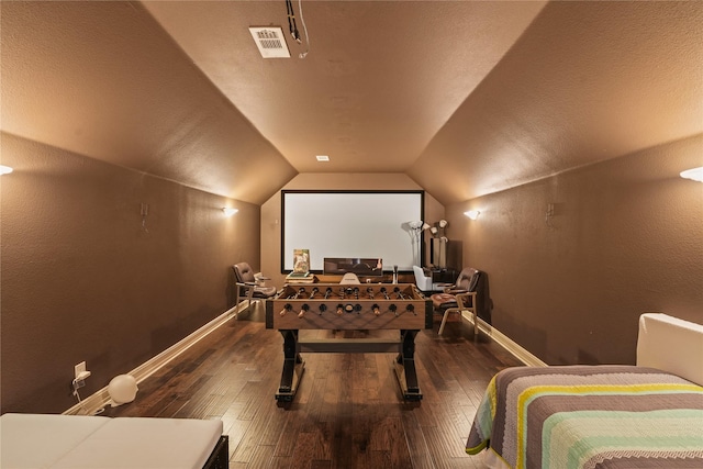 home theater room with baseboards, vaulted ceiling, visible vents, and hardwood / wood-style flooring