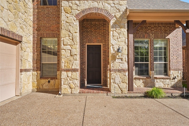 doorway to property featuring brick siding, a shingled roof, and stone siding