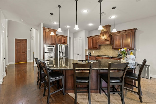 kitchen with baseboards, custom exhaust hood, a sink, decorative backsplash, and stainless steel appliances