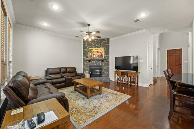 living room with a ceiling fan, a fireplace, visible vents, dark wood-type flooring, and ornamental molding