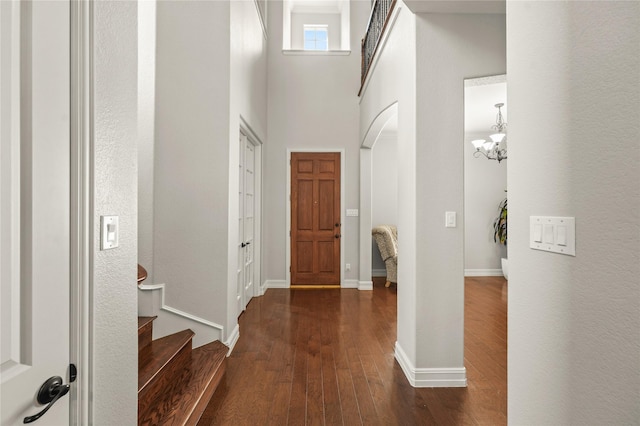entryway featuring a high ceiling, dark wood-type flooring, arched walkways, a chandelier, and stairs